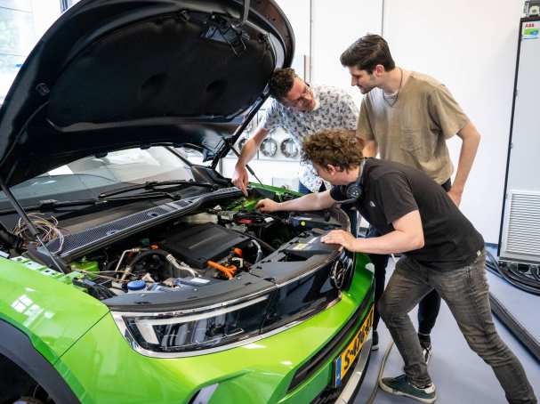 Studenten en docent automotive kijken naar de motor van de auto.