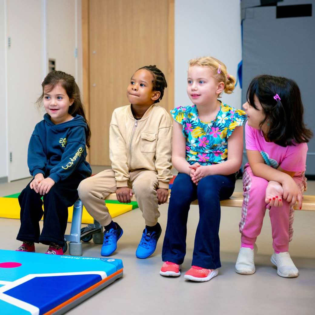 De kleuters op de school De Ommelander. Er zitten drie kleuters samen op een bankje.