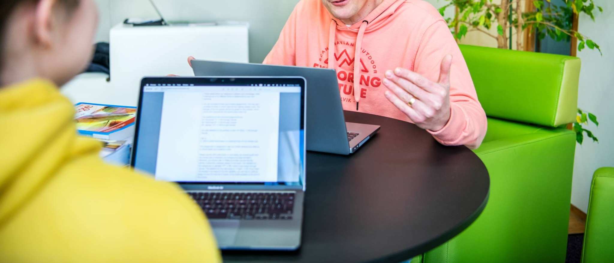 Foto Master Academie Educatie. 2 masterstudenten zitten aan een tafeltje op Kapittelweg 35 met hun laptops tegenover elkaar. Een van hen legt wat uit aan de ander.