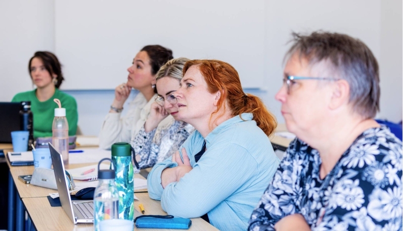 Vijf vrouwen in klaslokaal luisteren naar uitleg docent bij de opleiding technische thuiszorgverpleegkundige.