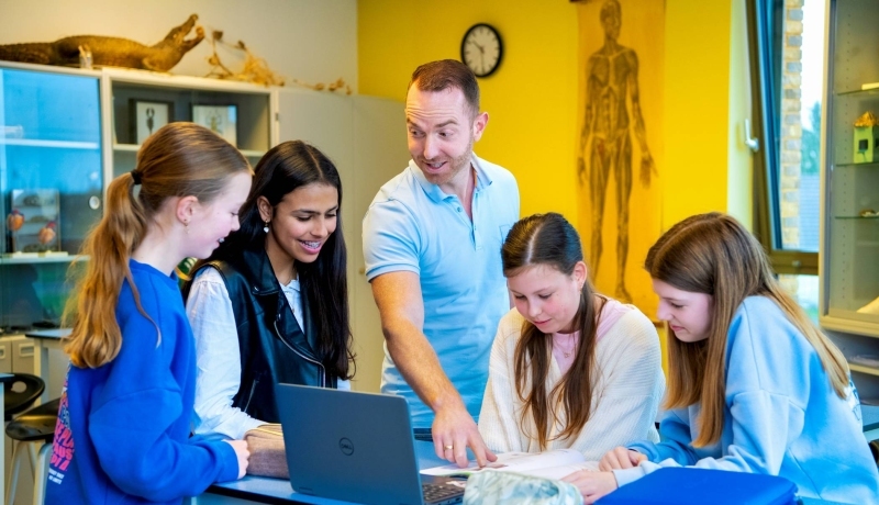 Docent Niels Janssen legt wat uit bij een laptop op tafel met 4 leerlingen op het Citadel College. 