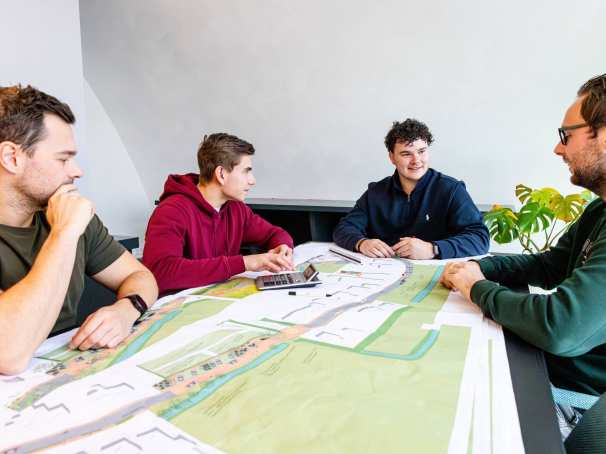 Vier mannen tijdens een bouwoverleg aan een bureau met daarop een omgevingskaart.