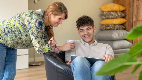 Moeder en zoon lachen terwijl ze hangen in een stoel en bezig zijn op de laptop. 