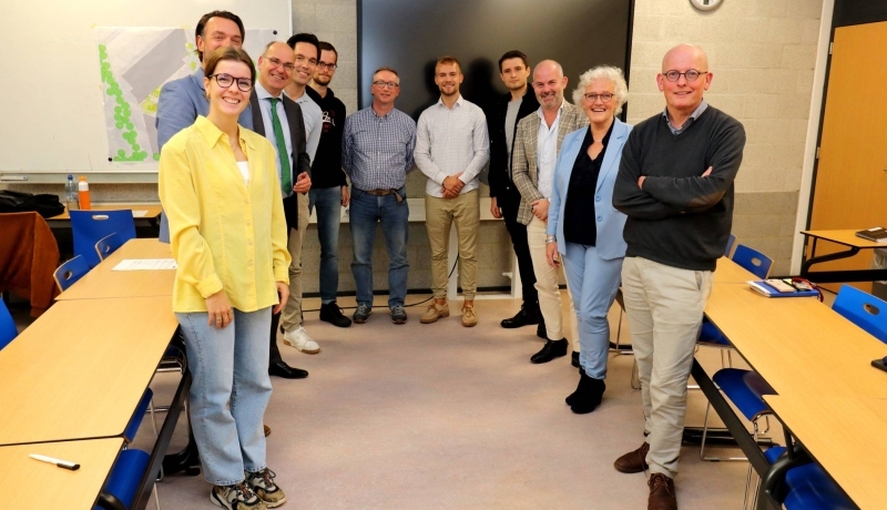 Drie studenten van de minor Circulaire Economie presenteren het plan Circular Square aan verschillende stakeholders. Er staan 11 mensen op de foto, die genomen is na het houden en bespreken van de presentatie. Lokaal op R31.