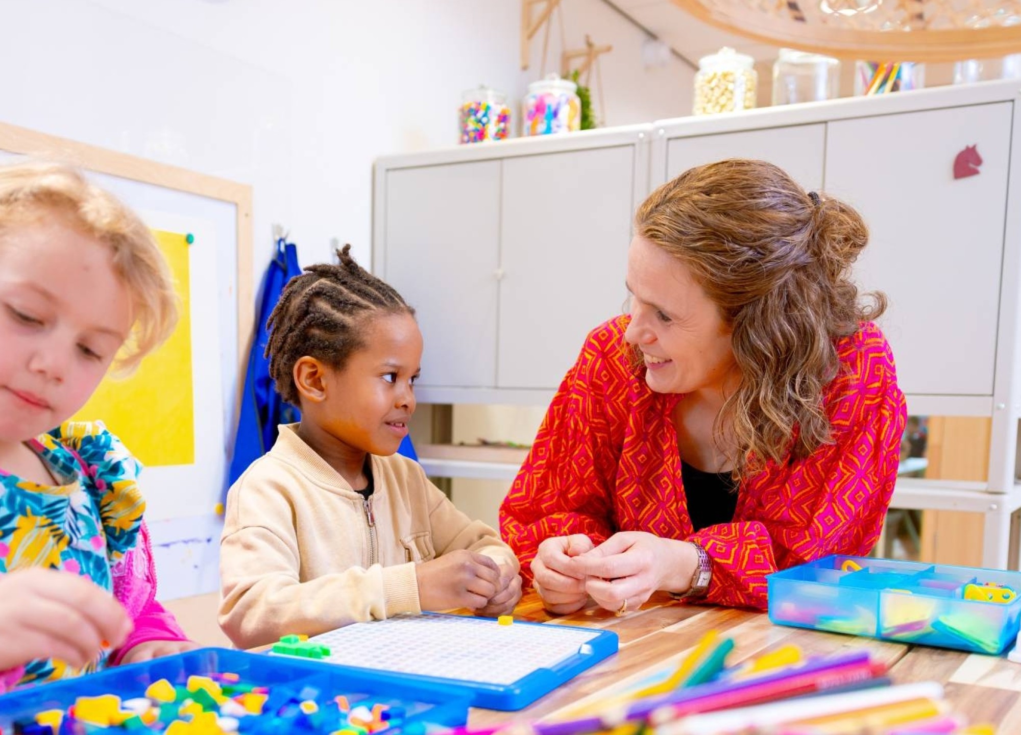 Omscholer naar basisonderwijs legt iets uit aan een kleuter in de klas.