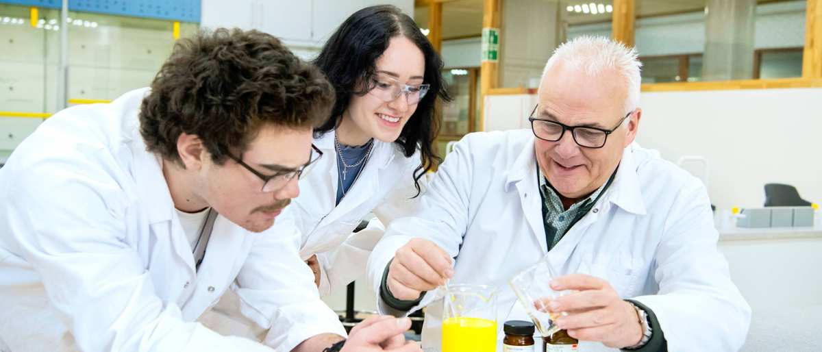 Twee studenten voeren met docent een proef uit in het lab
