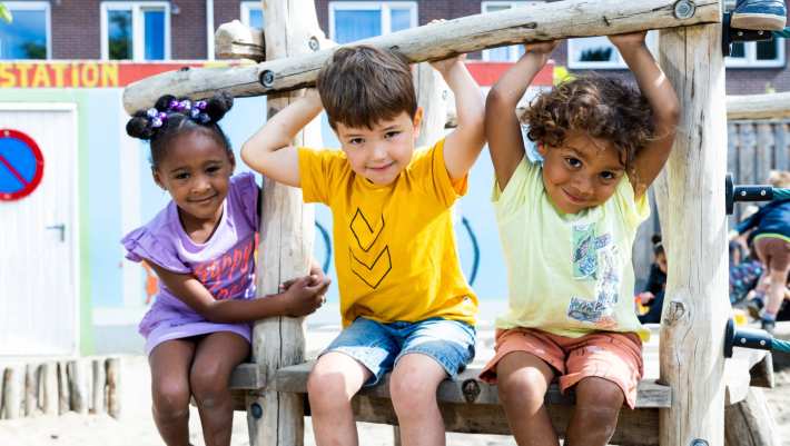 Drie kinderen spelen buiten en hangen aan het klimrek