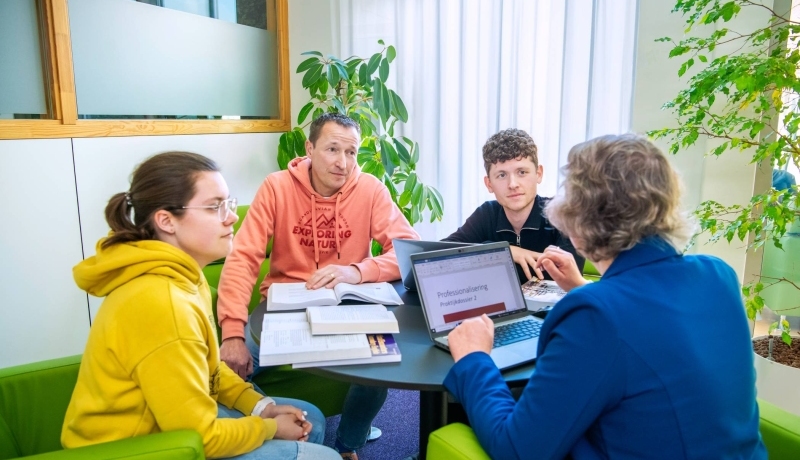 Foto Master Academie Educatie. 4 masterstudenten zitten om een tafel en overleggen samen. 