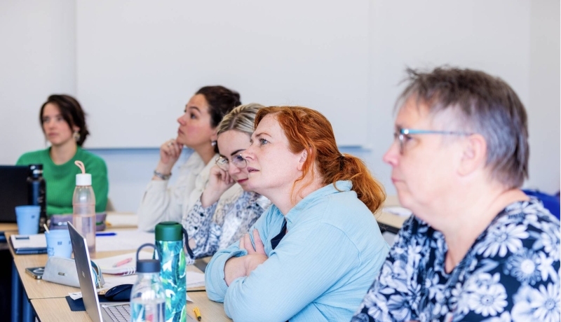 Vijf vrouwen in klaslokaal luisteren naar uitleg docent bij de opleiding technische thuiszorgverpleegkundige.
