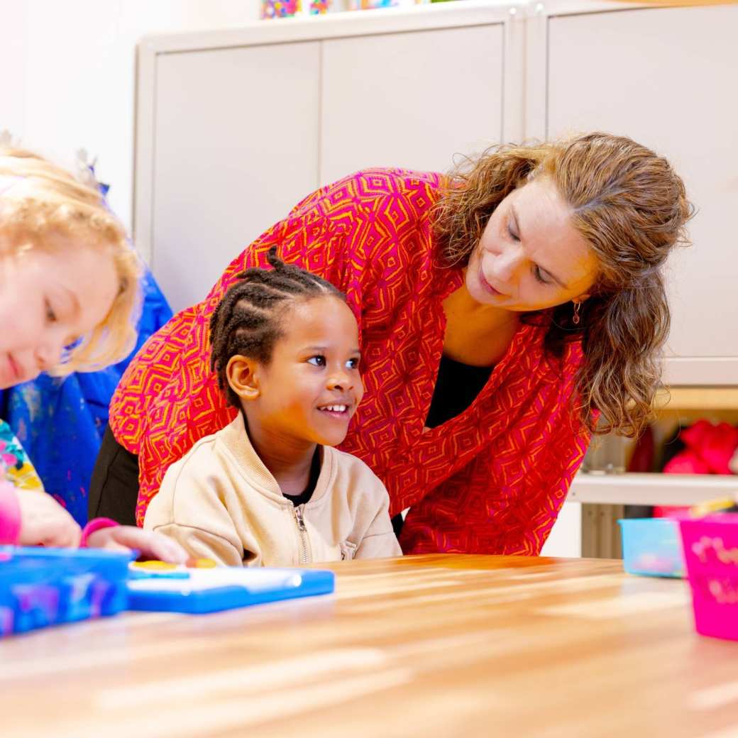 De kleuters op de school De Ommelander. De juf kijkt naar een kleuter aan de tafel.