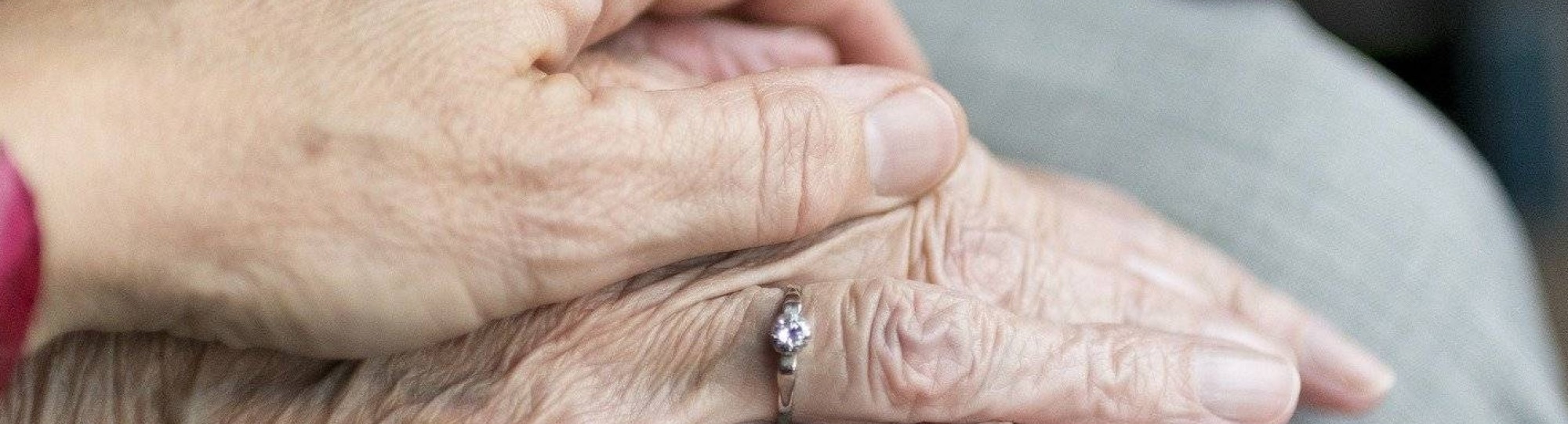handen oudere en verzorger in beeld