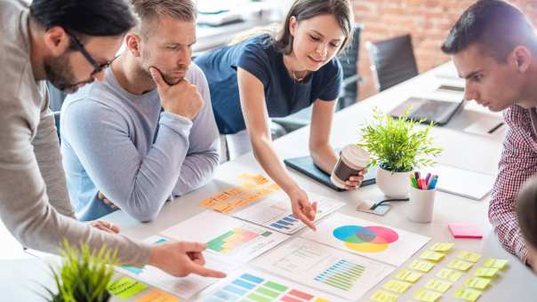 Sfeerbeeld van collega's die samenwerken aan een tafel met post-its, schema's en tabellen 