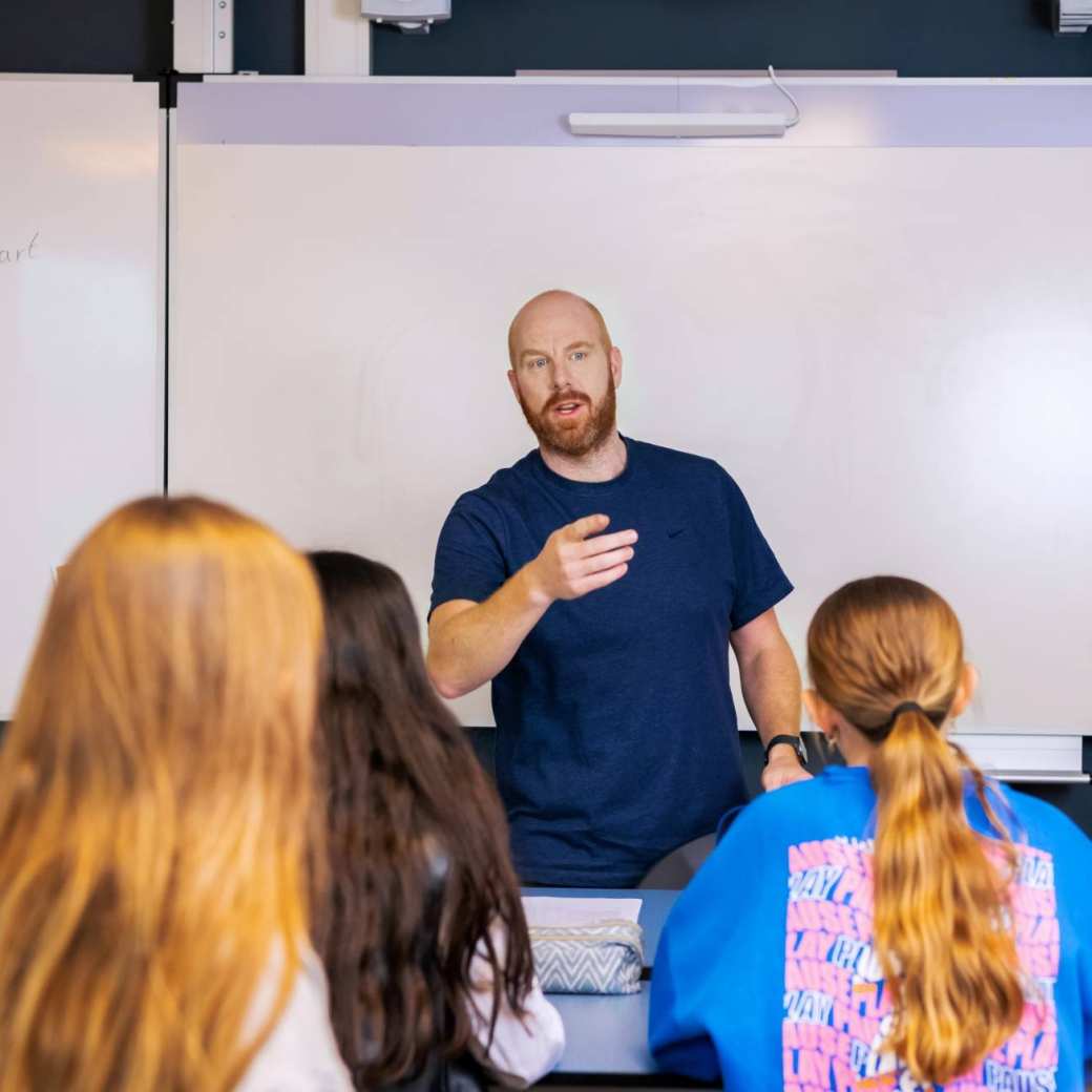 Fotoshoot op het Citadel 2024. Een mannelijke docent staat voor een groot whiteboard en legt wat uit, terwijl de scholieren naar hem luisteren