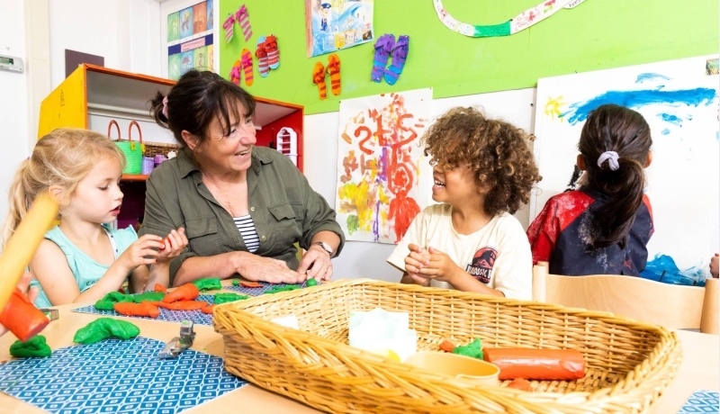 Lerares aan het werk op een basisschool samen met kinderen aan een tafel.