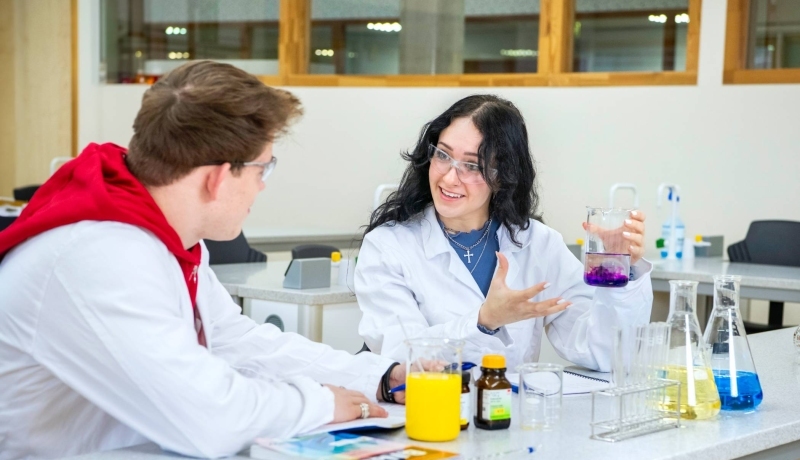 Twee studenten Leraar Scheikunde voeren een experiment uit en hebben een labjas aan en een veiligheidsbril op.