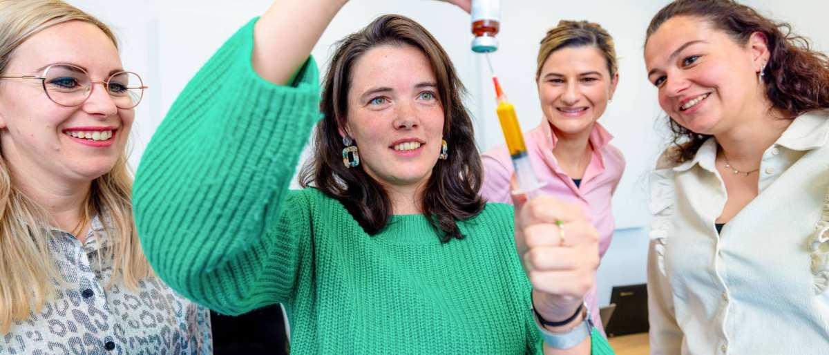 Student in groene trui heeft naald vast met potje met vloeistof. Tijdens de opleiding technische thuiszorgverpleegkundige. 