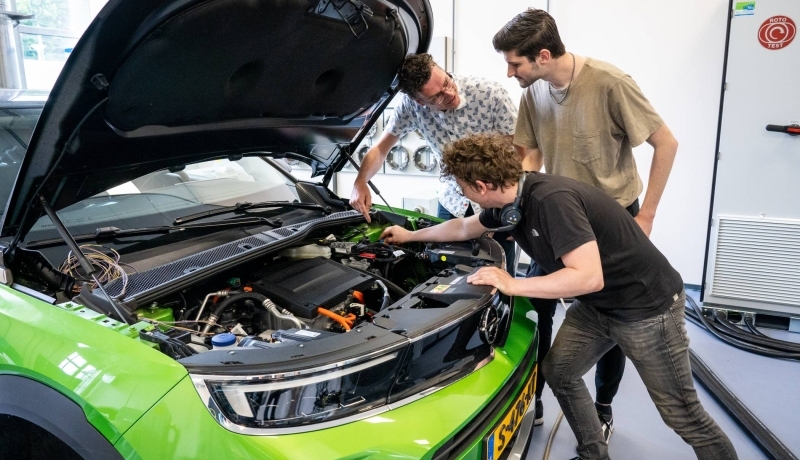 Studenten en docent automotive kijken naar de motor van de auto.