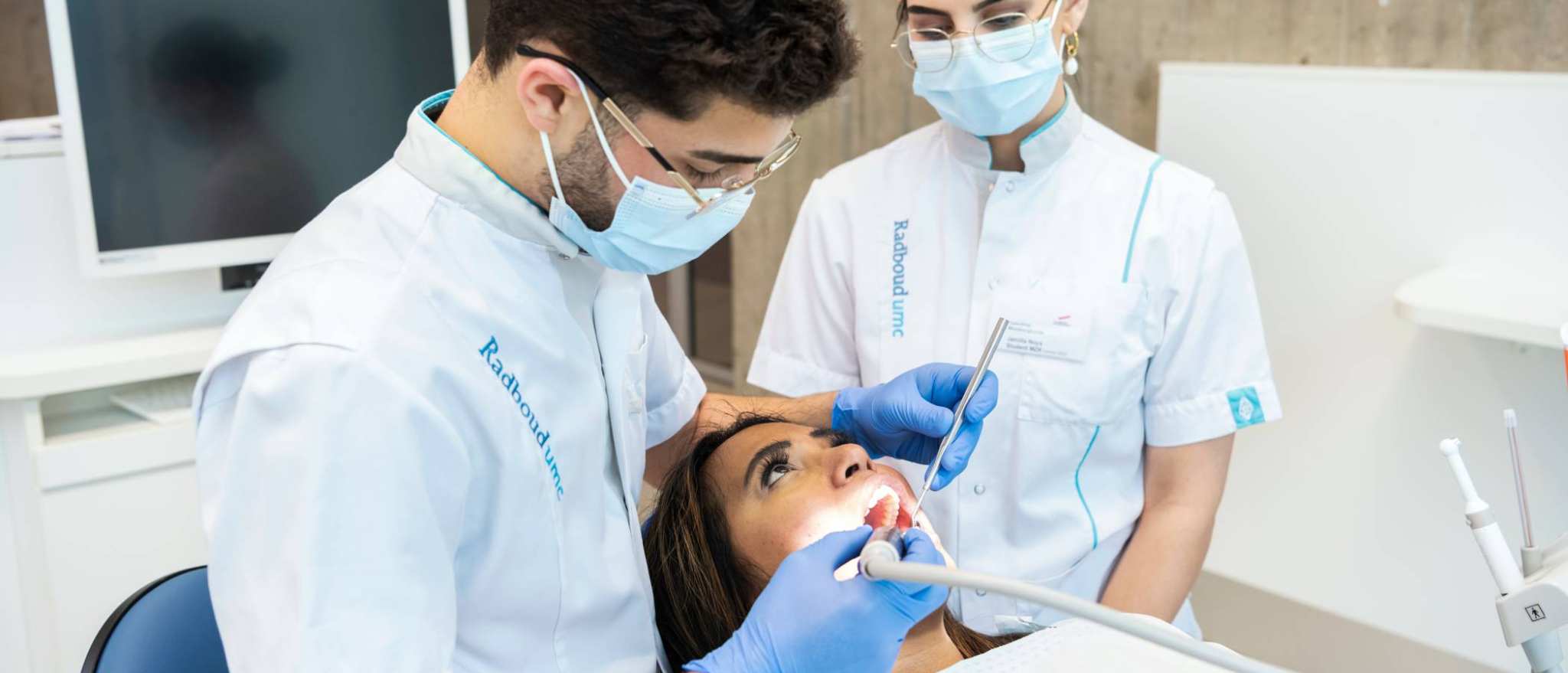2 studenten kijken in de mond van een patient. 1 heeft materialen vast, de ander kijkt toe.