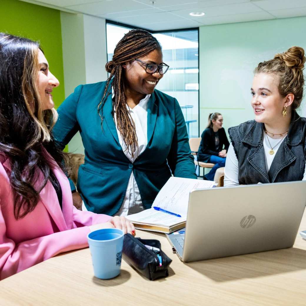 Studenten Human Resource Management (HRM) in gesprek met een docent met een laptop erbij