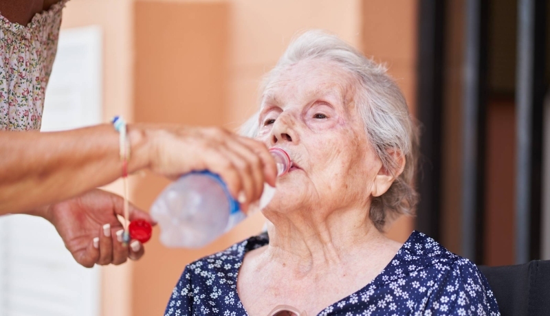 Een oude vrouw drinkt uit een flesje.