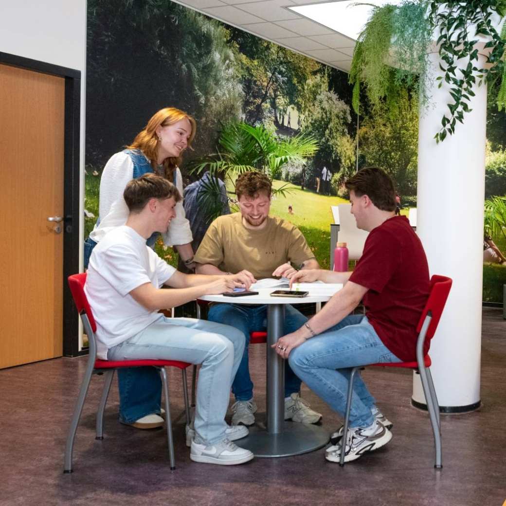 Studenten in gang bij Ergotherapie aan tafel overleggen met elkaar en 2 studenten komen in gang aanlopen.