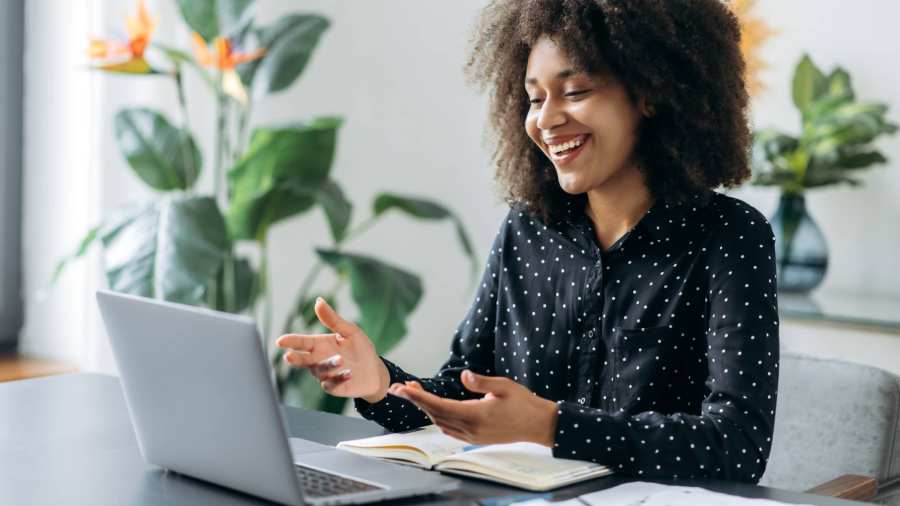Vrouw zit aan een bureau achter haar laptop. Ze heeft een online vergadering.