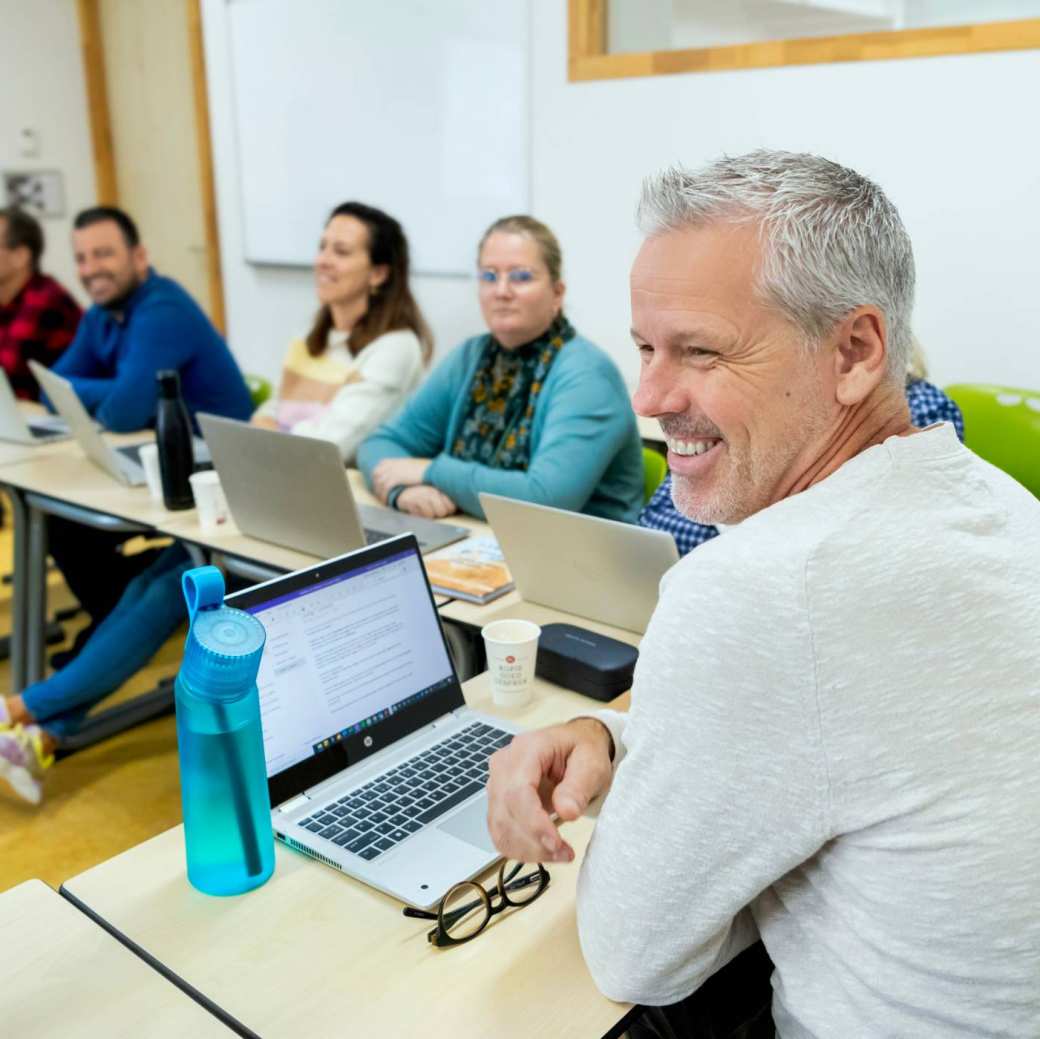 Foto van Master Ontwerpen van Eigentijds Leren. Een closeup van een lachende masterstudent in een lokaal, andere studenten vaag op de achtergrond in de klas.