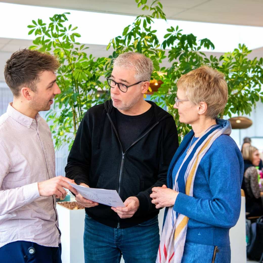 Student praat met docenten terwijl hij een blad vasthoudt. 