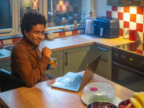 Man aan keukentafel met laptop en mok in hand