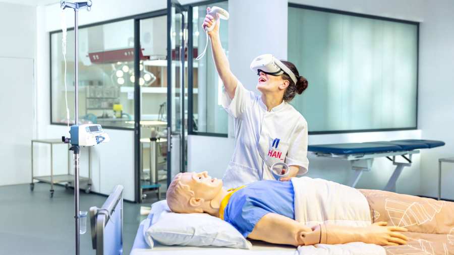 Verpleegkundige oefent met VR bril aan een ziekenhuisbed met dummy.