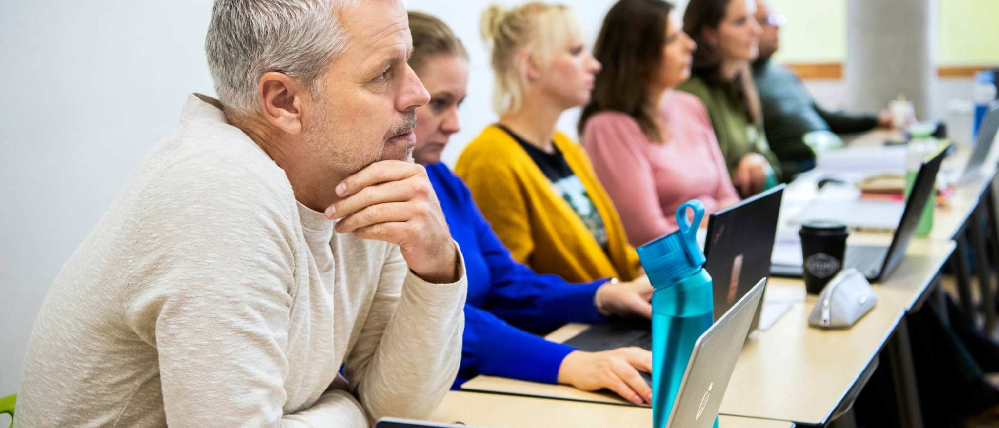 Foto van Master Ontwerpen van Eigentijds Leren. Close-up van één masterstudent die gefocust kijkt met andere masterstudenten vaag op de achtergrond.
