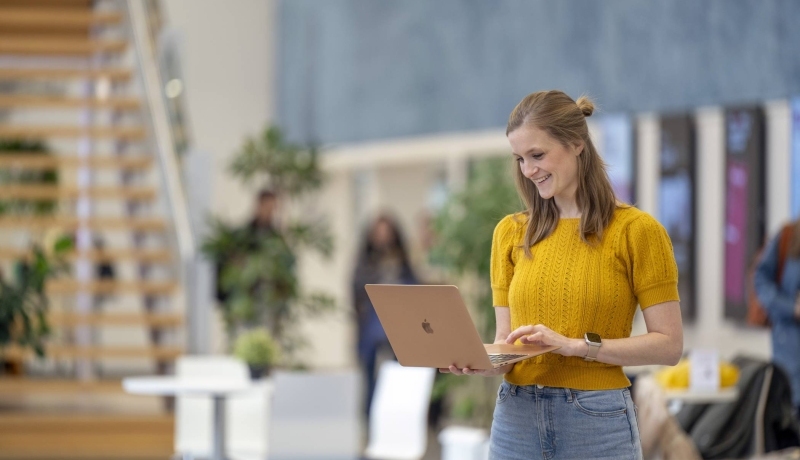 Deeltijdstudent checkt iets op haar laptop in de hal.
