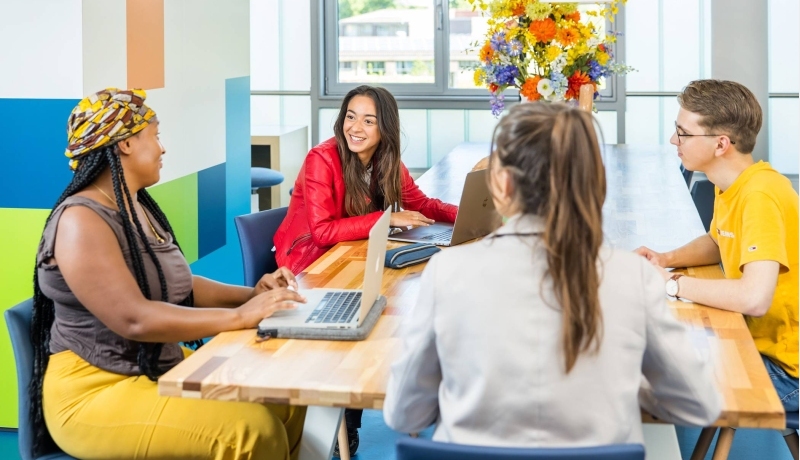 Lo-res. Groep van 4 studenten in overleg aan tafel in algemene ruimte HAN.