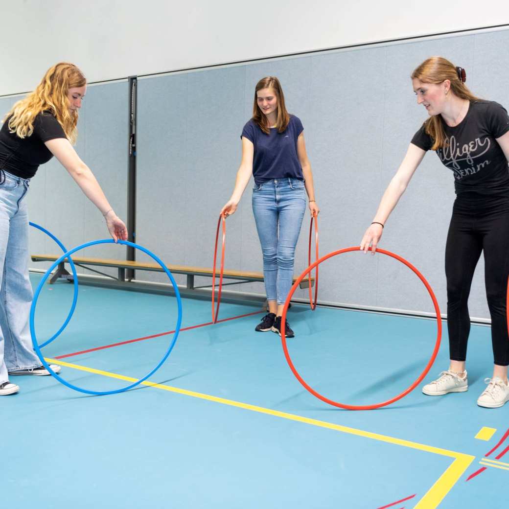 Studenten PMT doen een oefening met hoepels in gymzaal