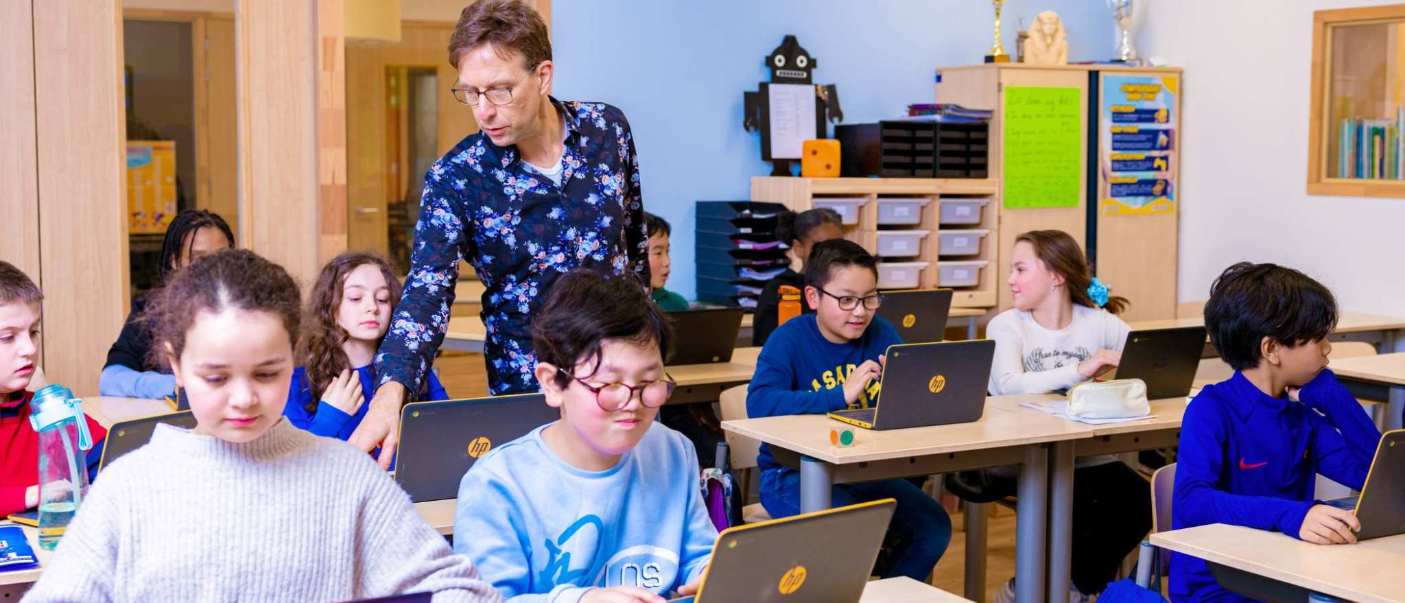 Groep 5,6,7 op de school Da Vince. De leerlingen zitten in de klas achter de laptop terwijl de leraar rond loopt. 