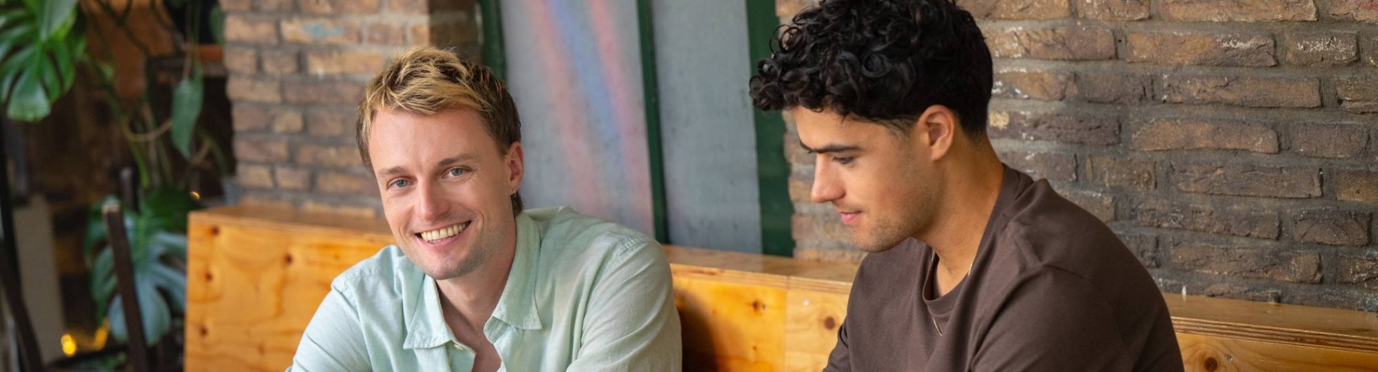 Twee studenten zitten aan tafel te studeren achter de laptop en lacht naar camera