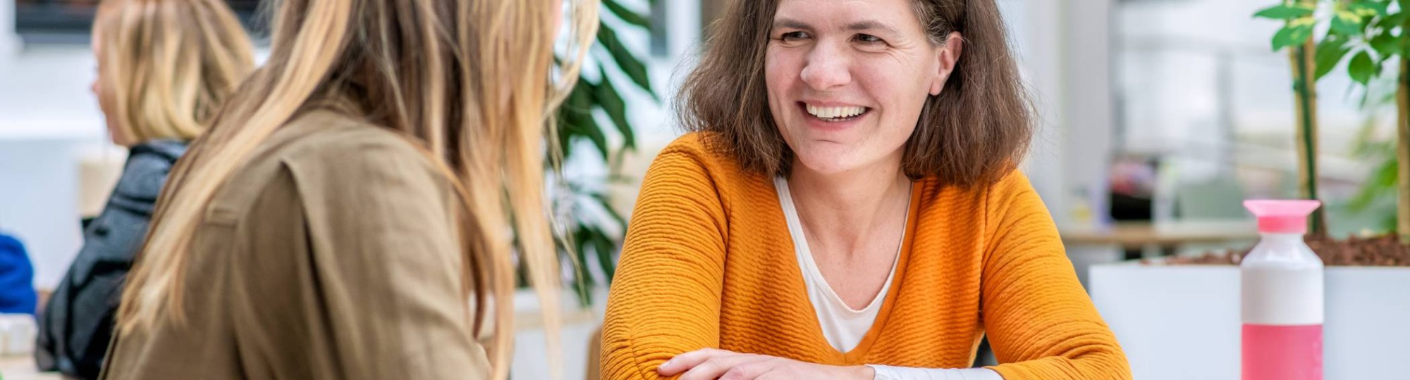 Vrouw in oranje trui lacht naar medestudent.