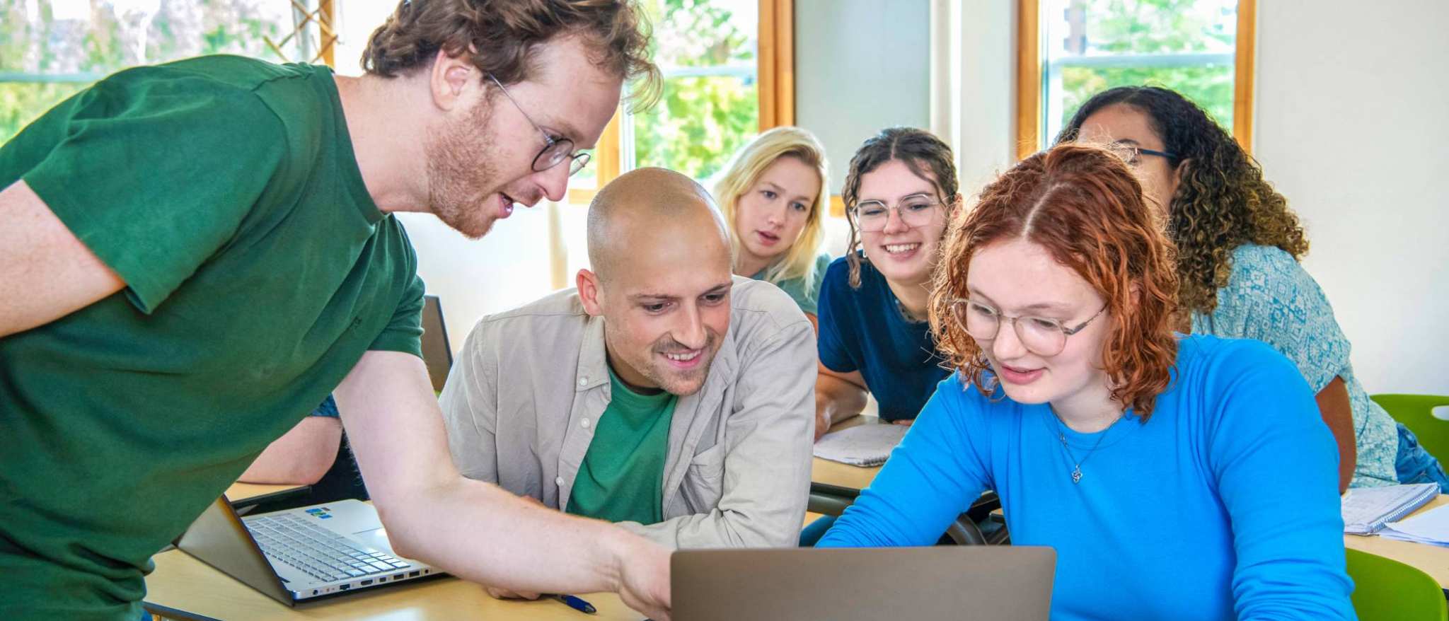 Leraar Wiskunde wijst iets aan op de laptop en klas kijkt van achter nieuwsgierig mee