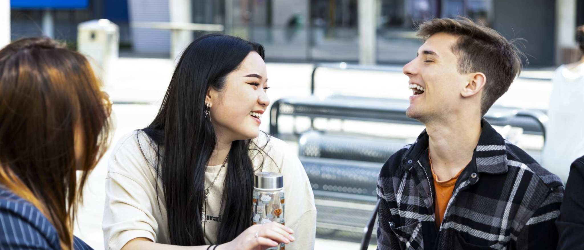 3 lachende studenten aan een tafel buiten R31 