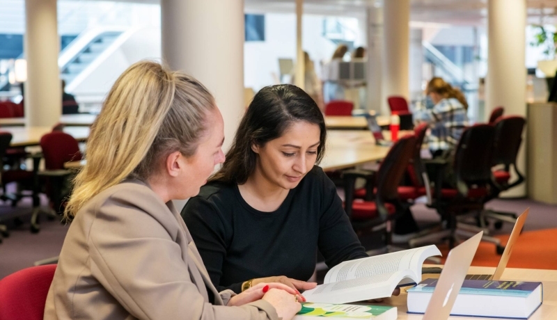 Twee studenten aan het werk in de bibliotheek en kijken naar een boek voor studie PMT deeltijd