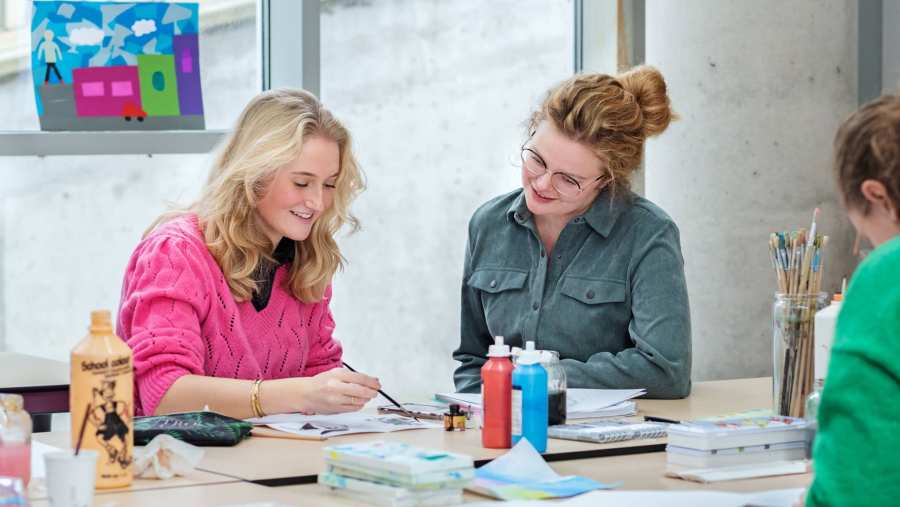 Fotoshoot maakdagen beeldende vorming 2022. Docente kijkt mee met studente tijdens het schilderen