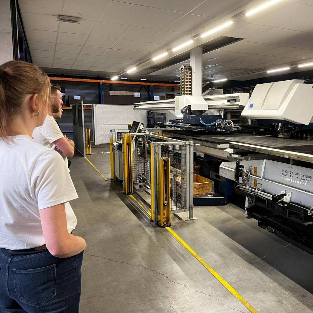 Sfeerbeeld van werkvloer tijdens bedrijfsbezoek bij Goma. Deelnemers kijken naar plaatbewerking.