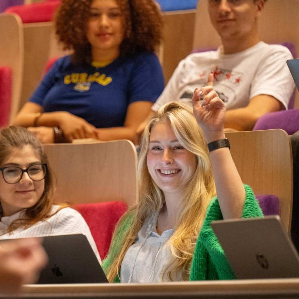 Studente steekt hand op tijdens hoorcollege in de collegezaal