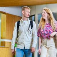 Twee studenten kijken lachend naar hun docent die tegenover hen zit.