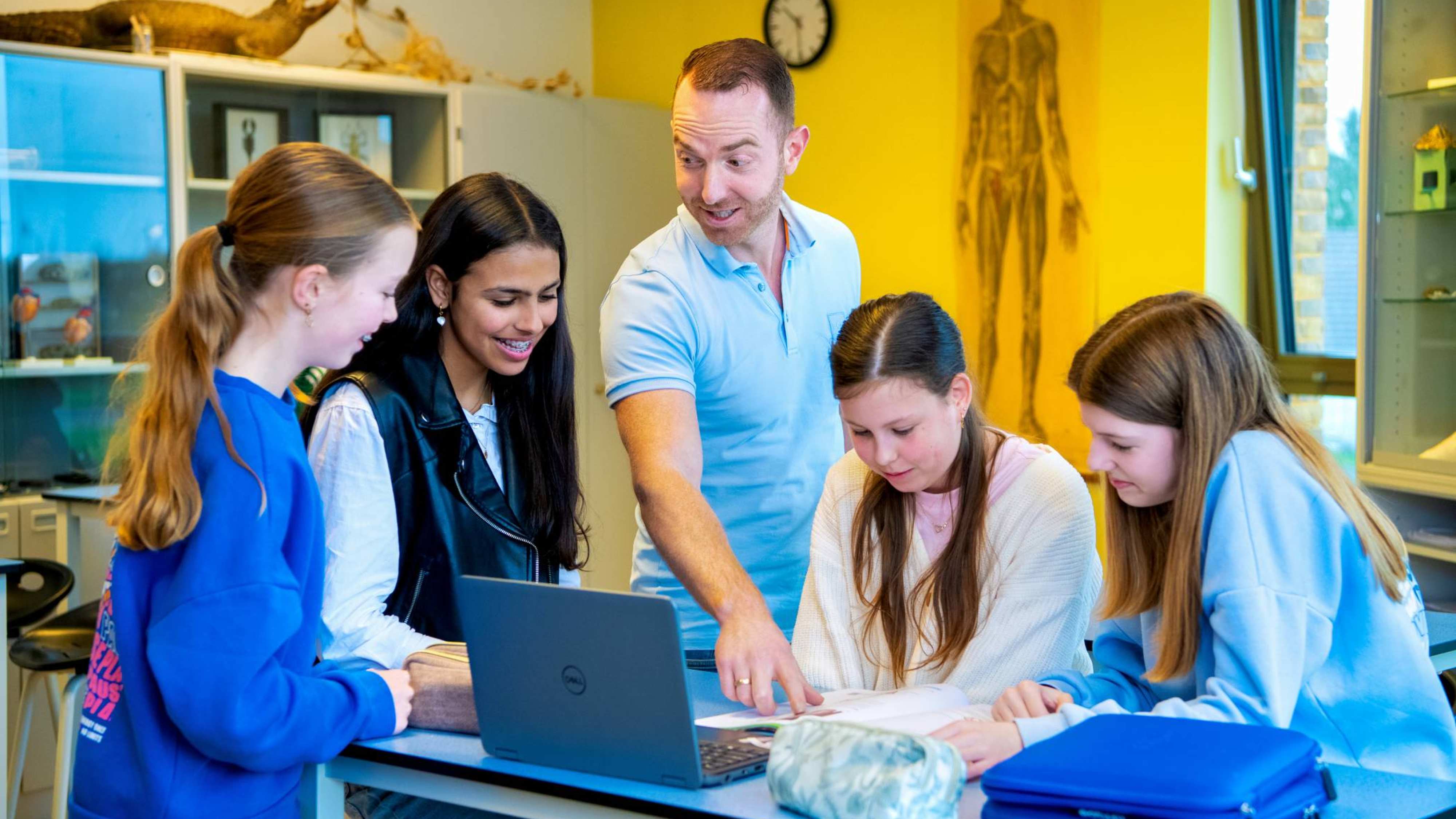Docent Niels Janssen legt wat uit bij een laptop op tafel met 4 leerlingen op het Citadel College. 