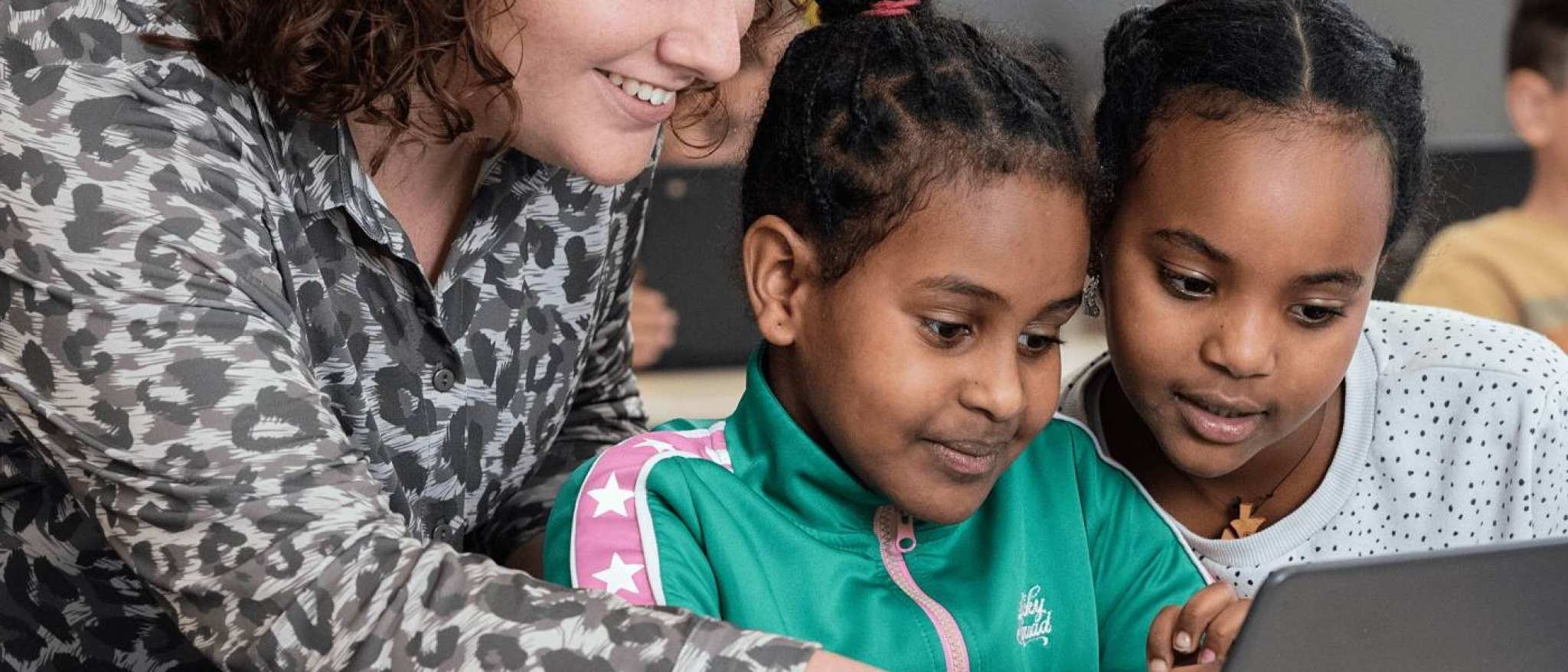Associate Degree Pedagogisch Educatief Professional wijst wat aan op laptop voor twee leerlingen