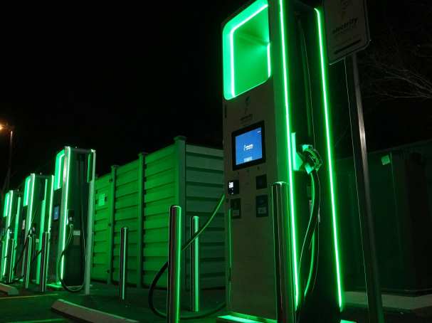 Foto met daarop groen verlicht elektrisch laadstation. Op een van de units staat electrify america