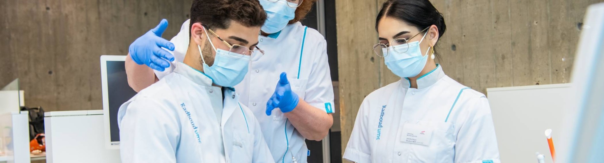 Docent helpt een student tijdens een behandeling, een andere student kijkt toe.