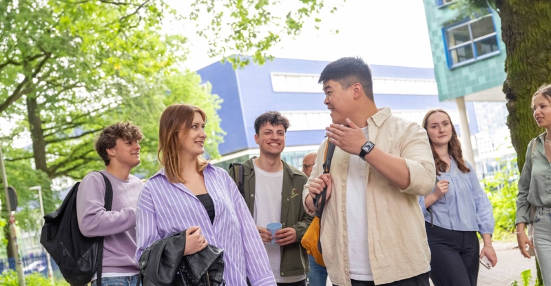 Groepje studenten staan buiten, met elkaar aan het kletsen, op de campus.