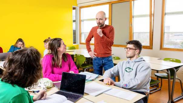Student geeft uitleg in een lokaal met gele muur